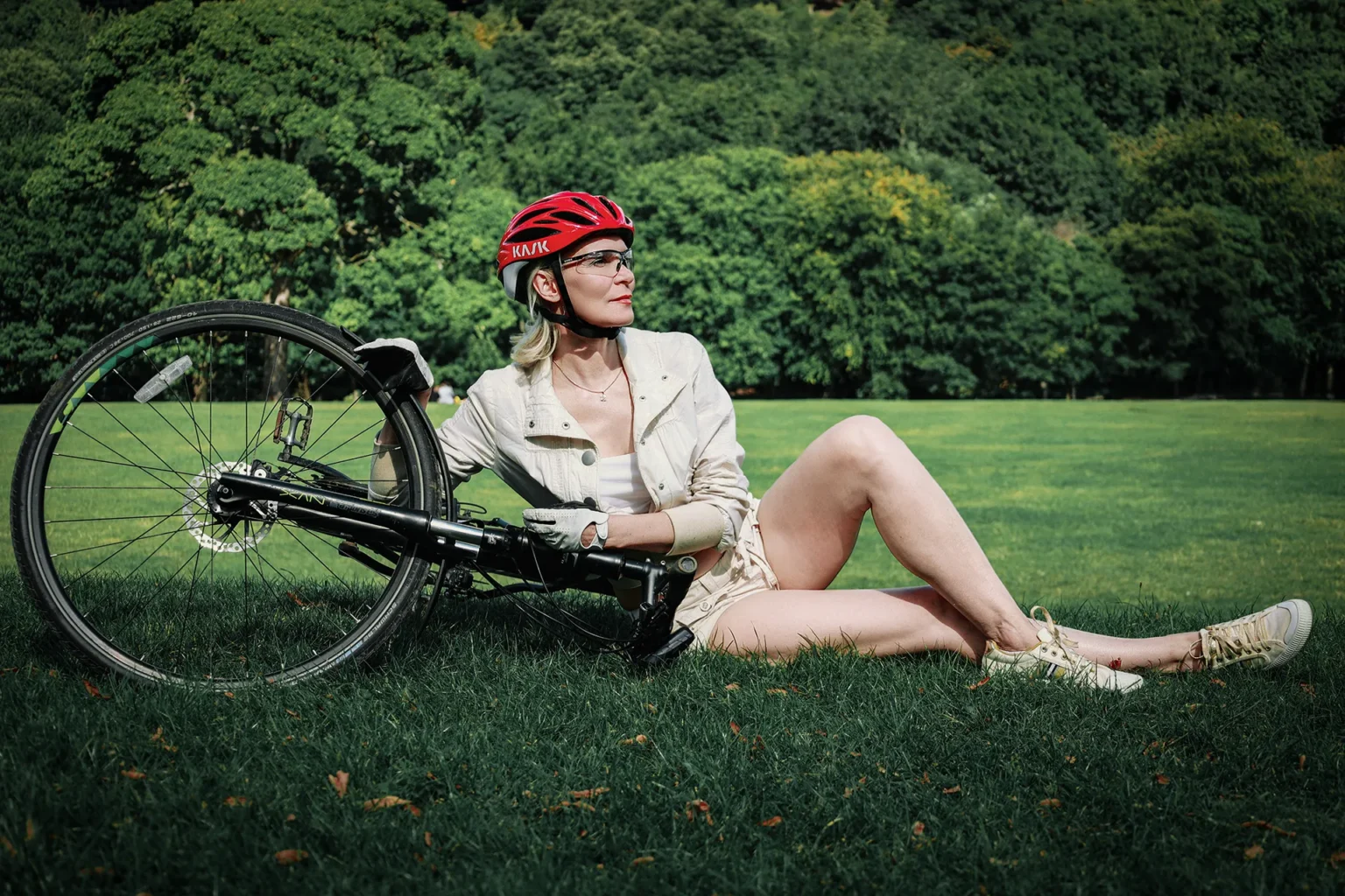 Woman in a red cycling helmet and light-colored clothing with a bicycle on grass during a Halifax outdoor photoshoot.